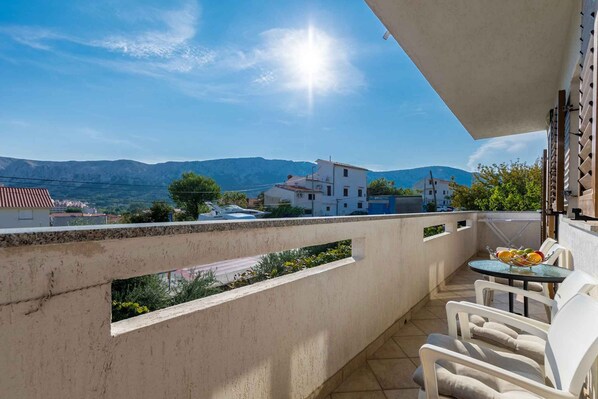 A balcony with a table and chairs, overlooking a mountainous landscape.