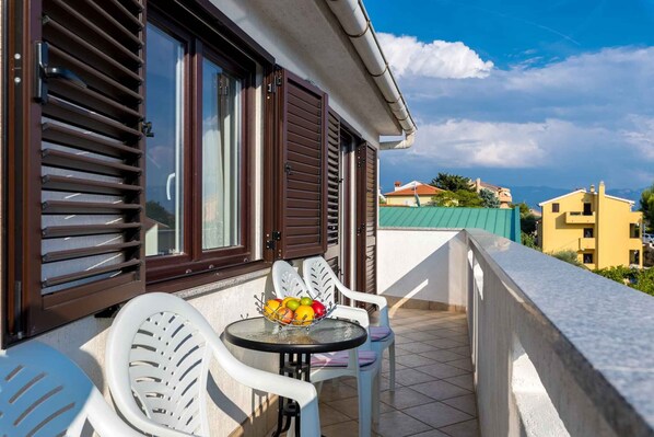 A balcony with a table and chairs, a bowl of fruit, and a view of buildings in the background.