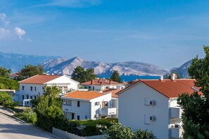 A coastal residential area with white buildings and red roofs, surrounded by mountains and a clear blue sky.