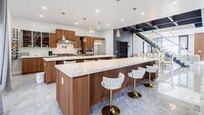 Et moderne køkken med en central ø, barstole og en trappe, der fører op til en etage.