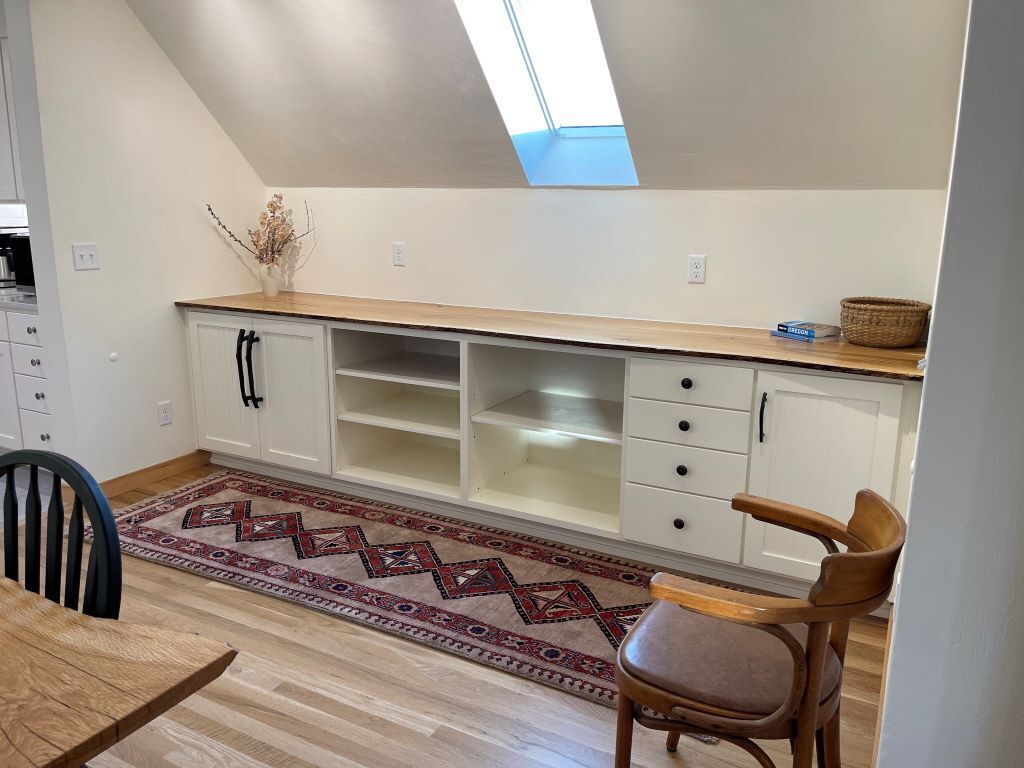 A kitchen with a skylight, wooden cabinets, a dining table, and a patterned rug.