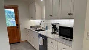 Una cocina moderna con armarios blancos, un lavamanos de acero inoxidable, una cafetera y un microondas.