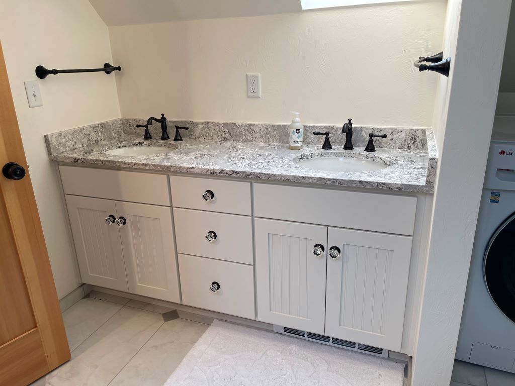 A bathroom with a double sink, white cabinets, and a washing machine.
