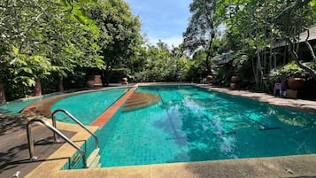 Una piscina con borde de azulejos, rodeada de exuberante vegetación y una terraza de madera.