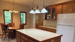 Une cuisine avec des meubles de rangement en bois, un réfrigérateur blanc, une table à manger avec des chaises et des luminaires suspendus.
