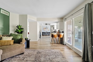 A modern living room with a sofa, a coffee table, and a rug. There is a dining area with a table and chairs in the background.