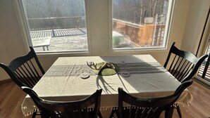 Un comedor con una mesa dispuesta para cuatro, ventanas amplias con vistas a montañas y un ventilador de techo.