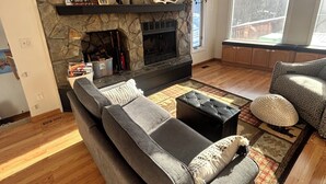Una sala de estar con chimenea de piedra, un sofá, una mesa de centro y un ventanal grande.