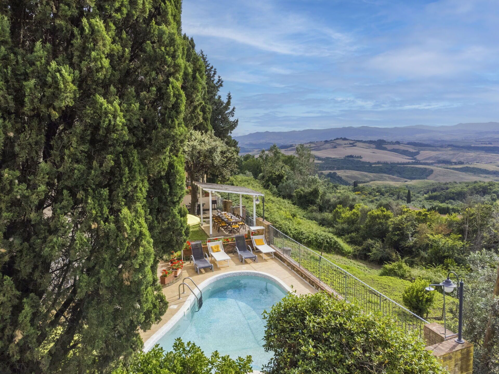 Ein Poolbereich mit Pergola, Liegestühlen und Blick auf sanfte Hügel.
