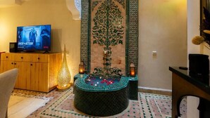 Een woonkamer met een televisie, een decoratieve wand, een klein fonteintje en een vloer met een patroon.