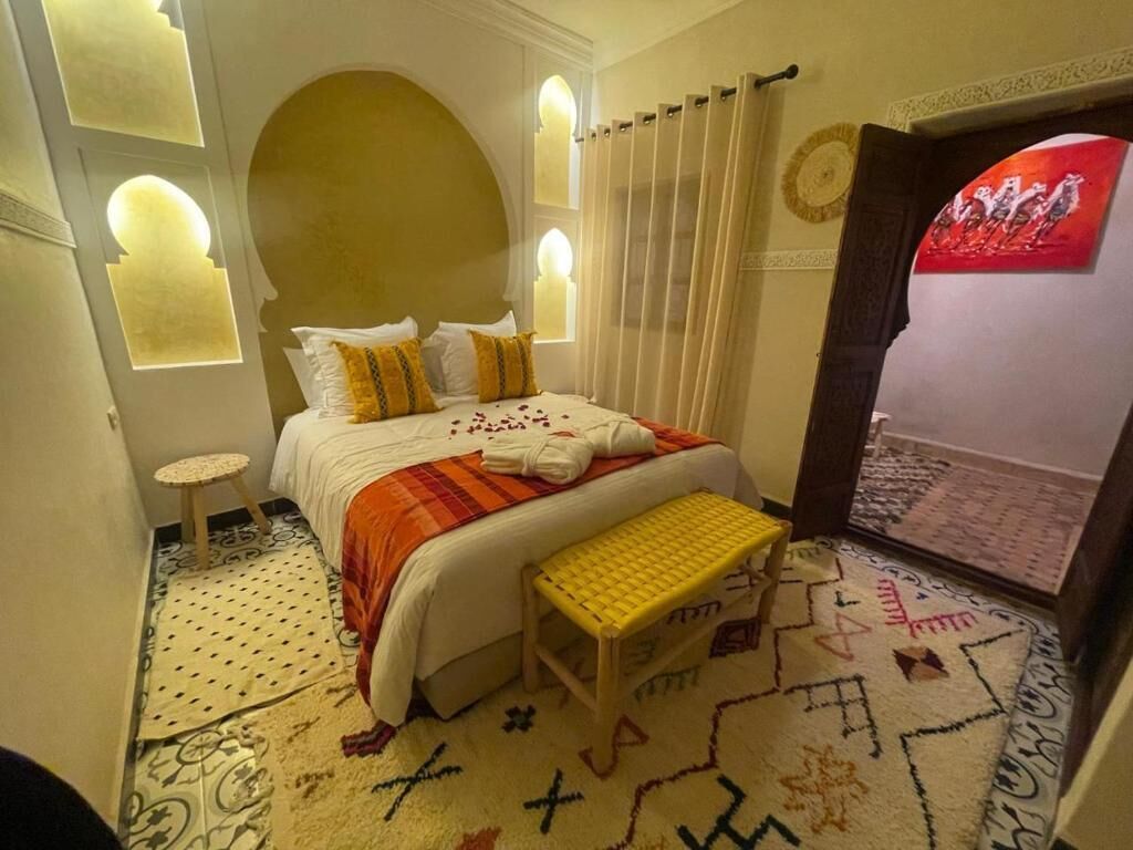 A hotel room with a bed, a small stool, a patterned rug, and a decorative wall.