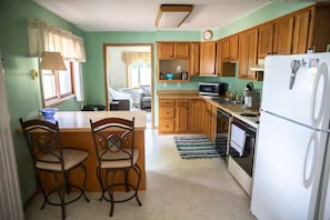A kitchen with wooden cabinets, a white refrigerator, a microwave, and a dining area with two chairs.