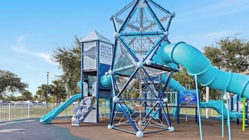 Un'area giochi con una struttura di arrampicata, scivoli e una casetta, con la scritta 'DESTIN FORT WALTON BEACH FLORIDA'.