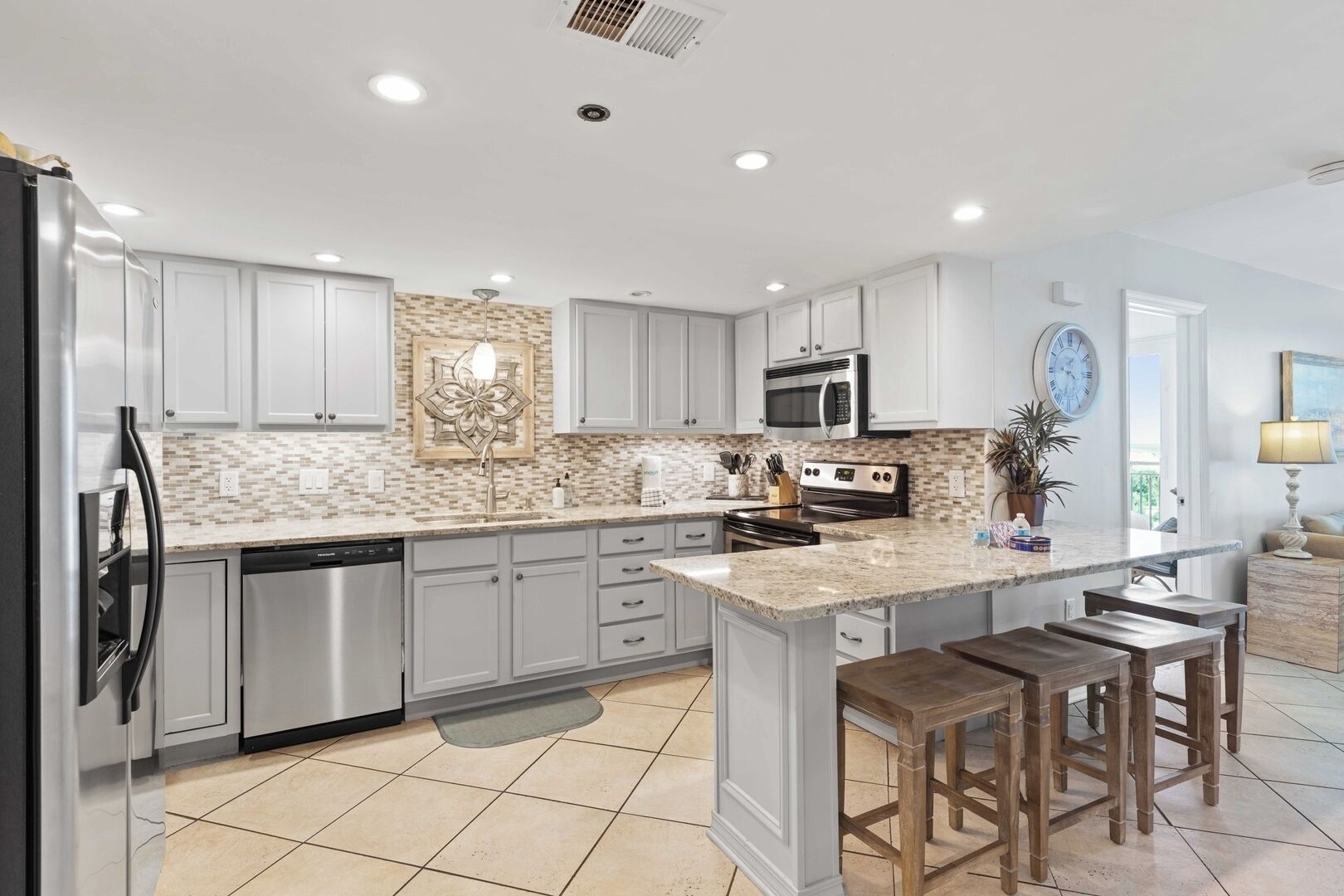 A modern kitchen with white cabinets, a granite countertop, stainless steel appliances, and a large island with stools.