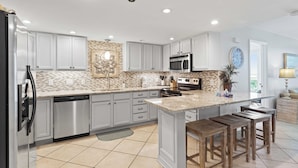 A modern kitchen with white cabinets, a granite countertop, stainless steel appliances, and a large island with stools.