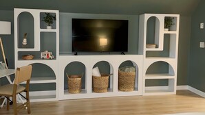 A bedroom with a bed, a TV mounted on a white entertainment unit, a ceiling fan, and a desk with a chair.