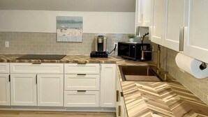 A kitchen with white cabinets, a herringbone-patterned countertop, and a microwave.