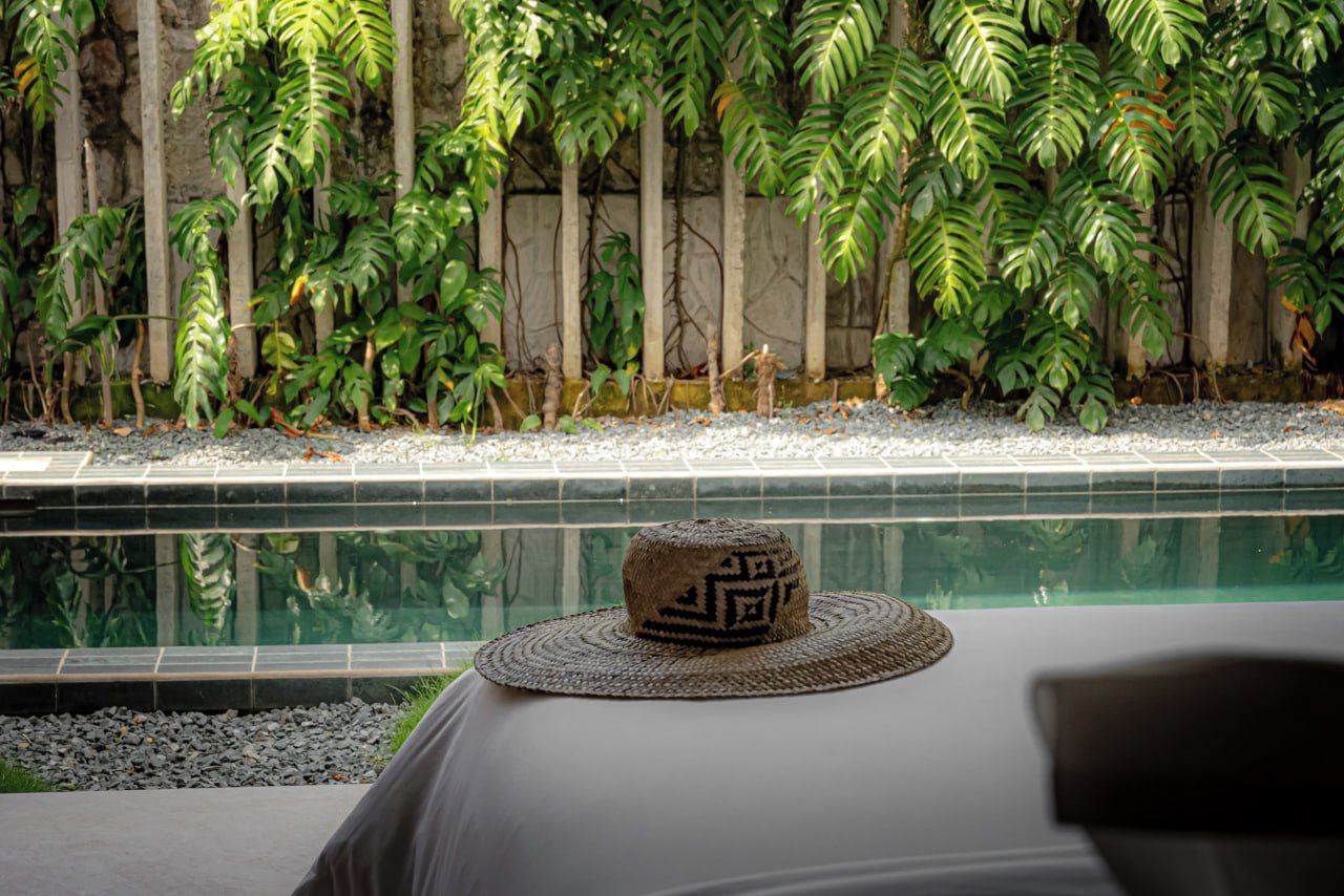 A hat on a table near a pool with a stone wall and green plants in the background.