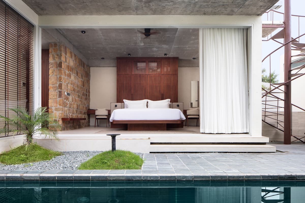 A modern bedroom with a large bed, a stone wall, and a view of a swimming pool.
