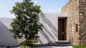 Un bâtiment moderne avec une façade en pierre, une porte en bois et un jardin bien entretenu agrémenté d’un arbre et de rochers.
