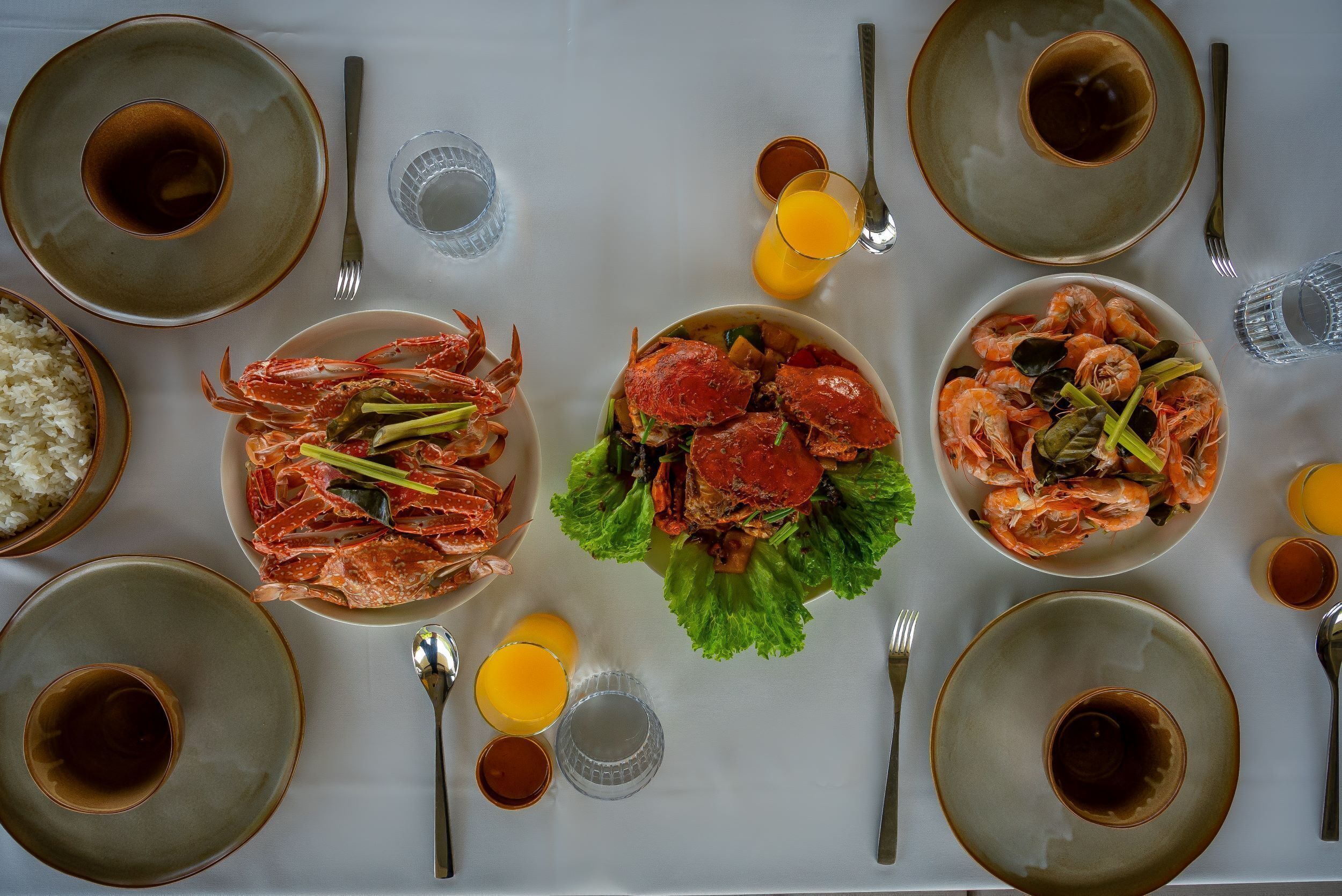 A dining table set with plates of seafood, bowls of rice, and glasses of orange juice.