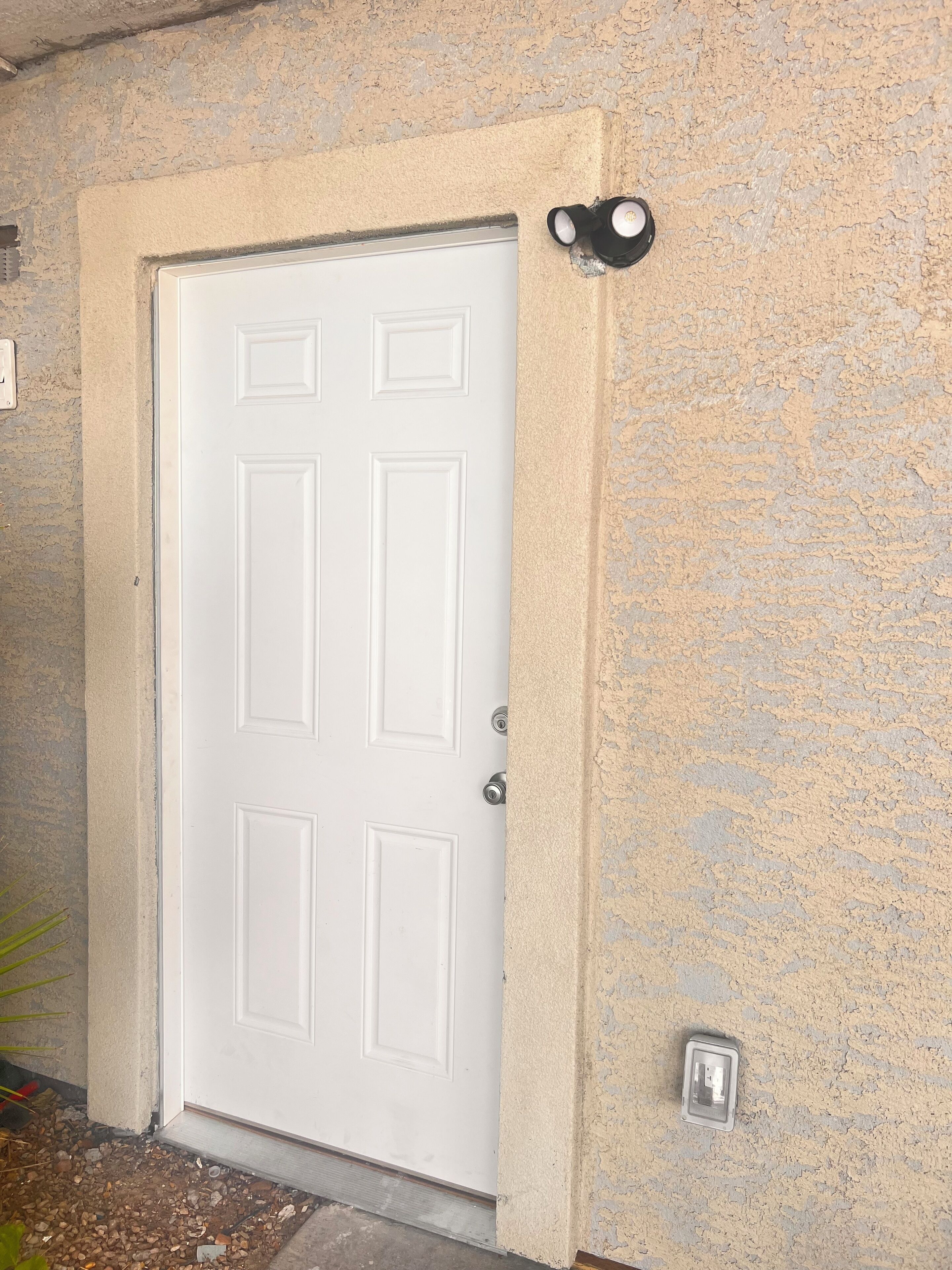 A white door with a textured beige wall, a small outdoor light fixture above it, and a security camera below.