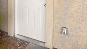 A white door with a textured beige wall, a small outdoor light fixture above it, and a security camera below. - Tranquil Beautiful Studio (Las Vegas)