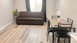 A living room with a brown sofa, a wooden dining table with four chairs, and a potted plant. - Tranquil Beautiful Studio (Las Vegas)