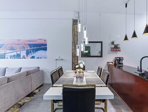Un espace de salle à manger moderne avec une table blanche, des chaises noires et des luminaires suspendus.