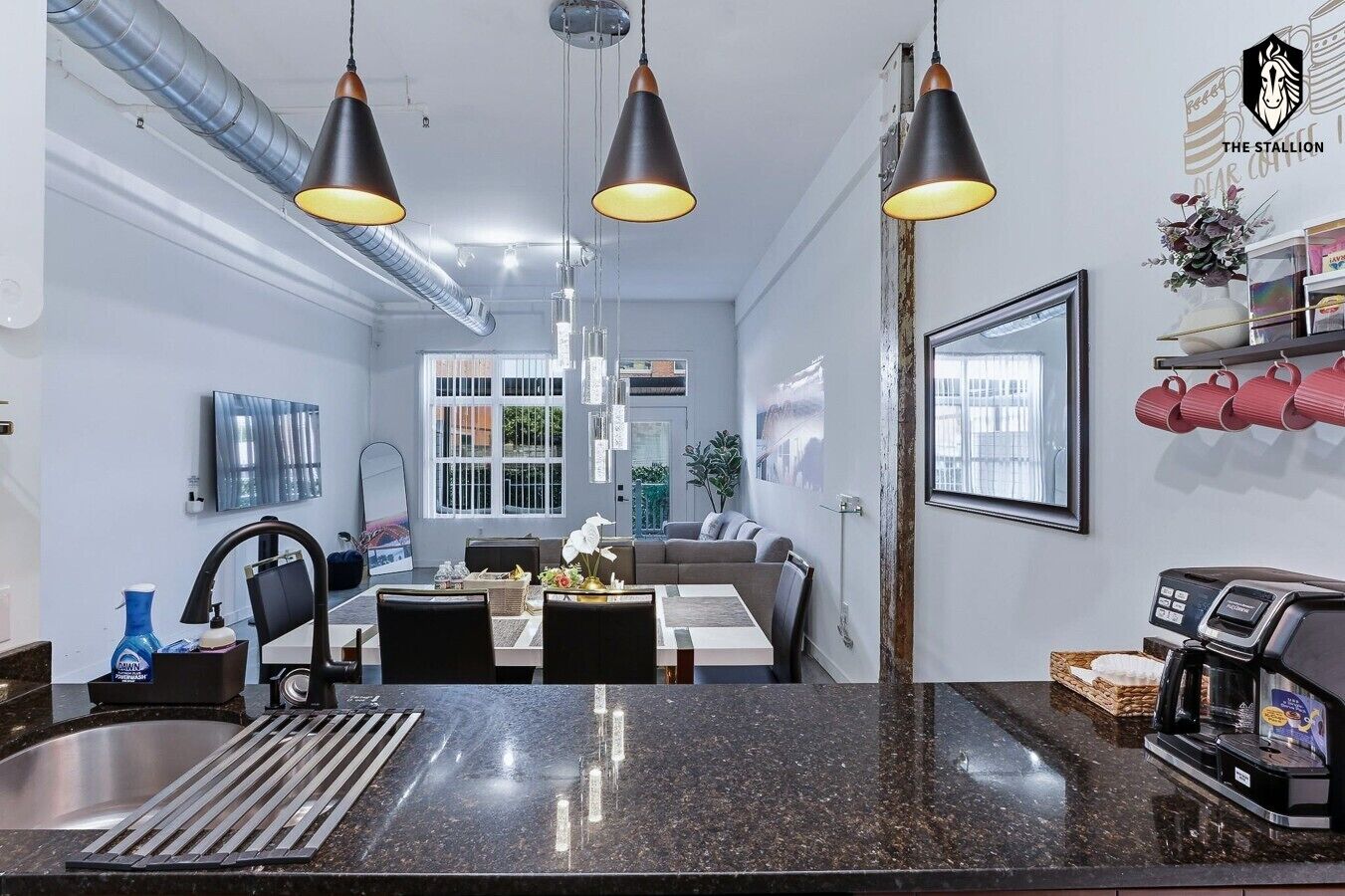 A modern kitchen with a granite countertop, a coffee machine, and pendant lighting.