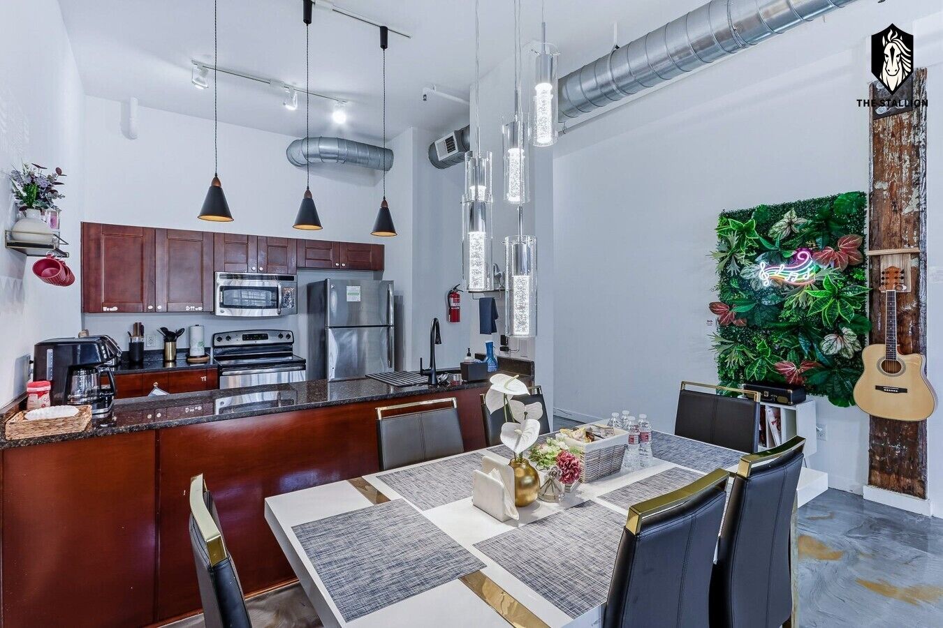 A modern kitchen with stainless steel appliances, a dining area with a marble table, and a decorative wall with plants and a guitar.
