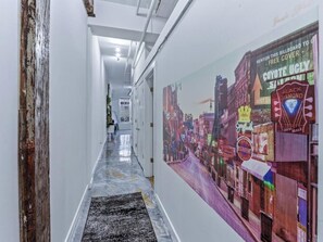 A corridor with a mural of a city street on the right wall, a black and white rug on the floor, and white walls with visible pipes. - Modern Spacious Loft in Downtown w/ free parking (Memphis)