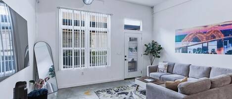A modern living room with a sofa, a coffee table, and a large window with blinds.