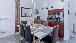 A modern kitchen with stainless steel appliances, a dining area with a white table and chairs, and pendant lighting.