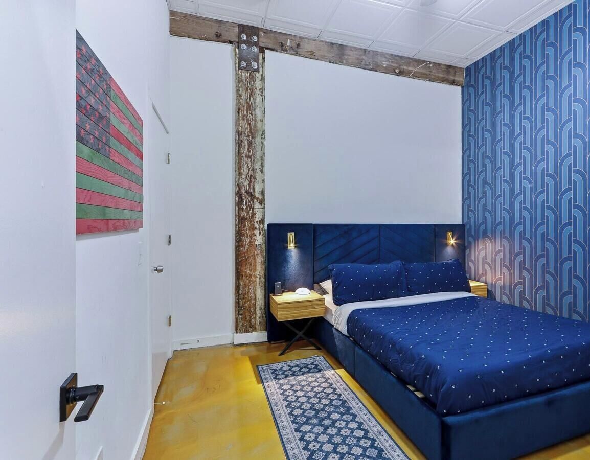 A bedroom with a bed, nightstands, a patterned rug, and a wall with a geometric design.