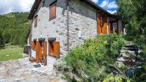 Una casa de pedra amb persianes de fusta, una escala de pedra i un paisatge de muntanyes al fons.