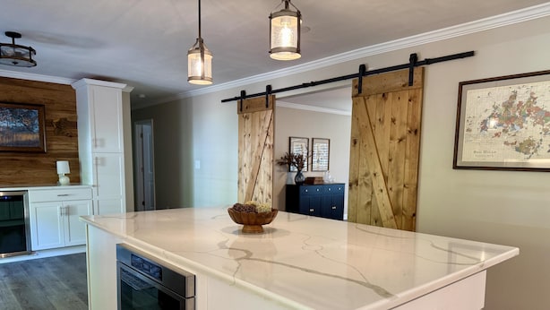 Una cocina con isla de mármol, muebles blancos y una lámpara colgante.