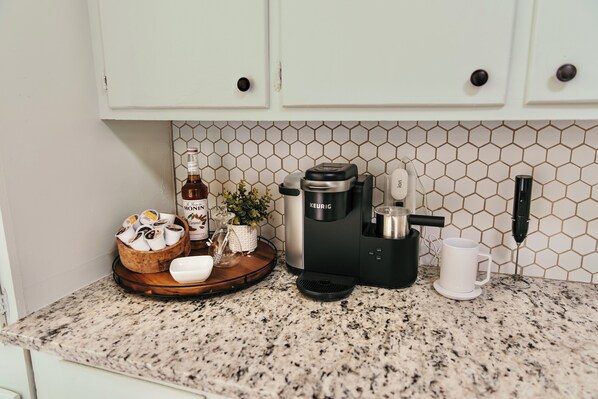 Un comptoir de cuisine avec une machine à café, une tasse, une bouteille et un bol rempli de capsules de café.
