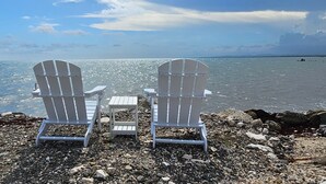 Duas cadeiras Adirondack de frente para uma orla rochosa, com vista para o oceano.