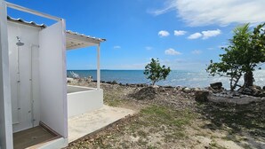 Um edifício branco com área externa coberta, vista para o mar e uma pequena árvore.