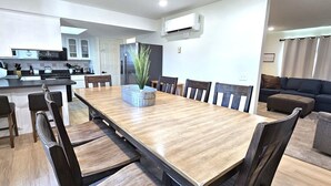A modern kitchen with a central island, a dining area with a long wooden table and chairs, and a living area with a sofa and ottoman. - Paddleboards, Air Hockey, Grill, Fire Pit, W/D, Brkfst, Sleeps 20 (Page)
