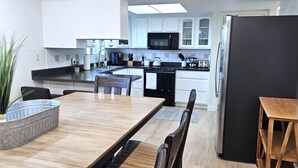 A modern kitchen with white cabinets, a black refrigerator, and a dining area with a wooden table and chairs. - Paddleboards, Air Hockey, Grill, Fire Pit, W/D, Brkfst, Sleeps 20 (Page)