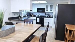 Une cuisine moderne avec des meubles blancs, un réfrigérateur noir et un coin repas comprenant une table et des chaises en bois.