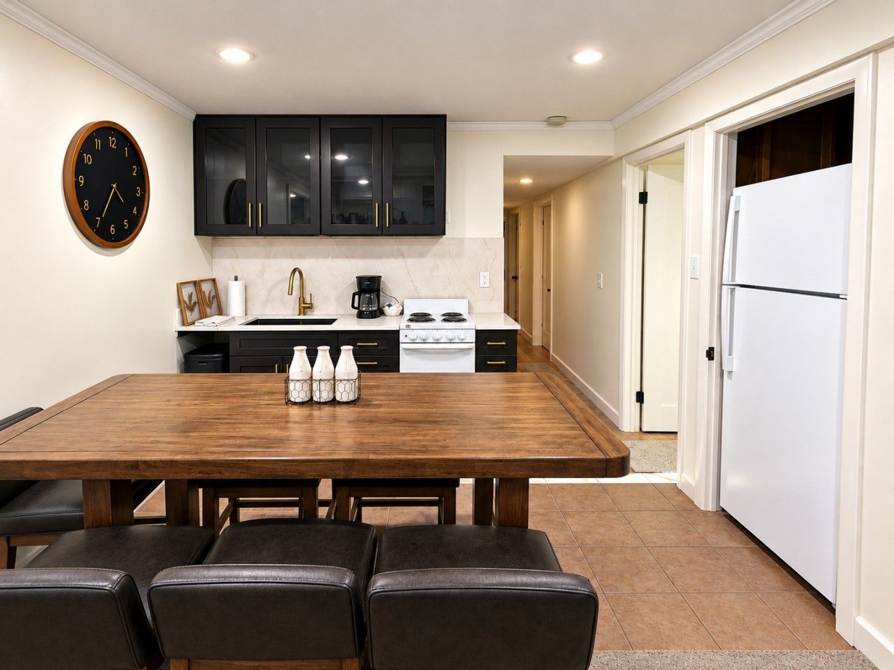 A modern kitchen with a wooden dining table, black cabinets, and a white refrigerator.