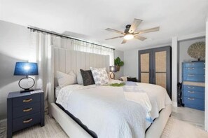 Un dormitorio con cama, mesita de noche, lámpara, ventilador de techo y un armario azul.