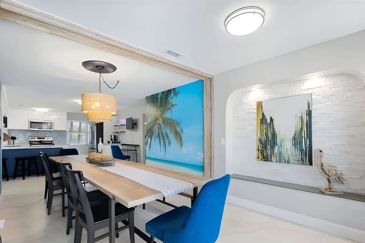 A modern dining area with a large painting of a beach, a cityscape, and a wooden sculpture on the wall.