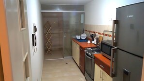 Eine kompakte Küche mit einem Bosch-Kühlschrank, einem Herd und einer Mikrowelle. Eine Holzleiter lehnt an der Wand und es gibt einen Spülbereich mit einer blauen Arbeitsplatte.