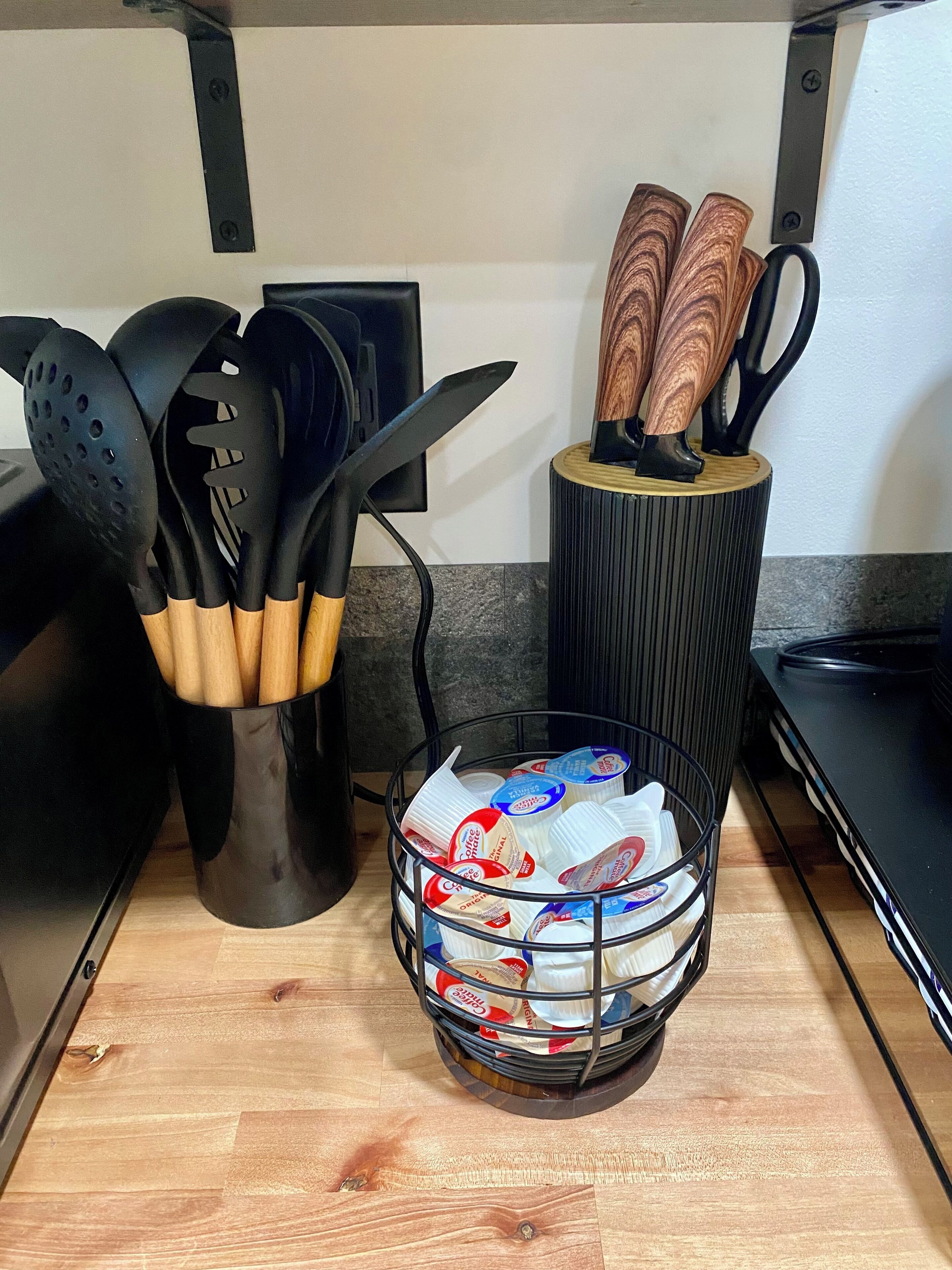 Un plan de travail de cuisine avec un porte-ustensiles, un panier de serviettes en papier et une paire de ciseaux.
