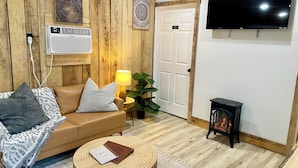 Un salon chaleureux avec un mur en bois, un téléviseur à écran plat, un canapé avec des coussins, une petite table basse ronde en bois, une lampe et une petite cheminée.