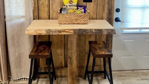 Une table en bois rustique, ornée d’un tableau représentant un coq, un panier rempli d’en-cas et deux tabourets.